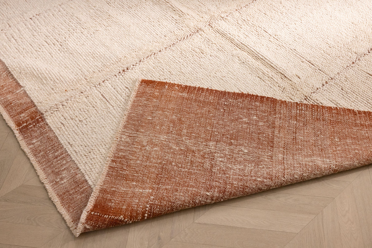 Handwoven terracotta and cream shaggy wool rug with a thick, textured pile and folded corner showing the durable backing.