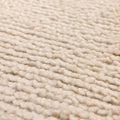 Close-up of a soft, cream-colored handwoven shaggy wool rug featuring a thick, textured high-pile weave.