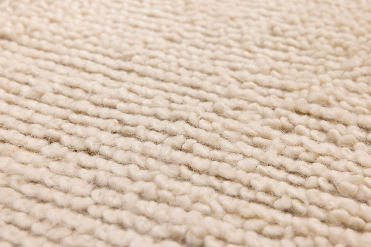 Close-up of a soft, cream-colored handwoven shaggy wool rug featuring a thick, textured high-pile weave.