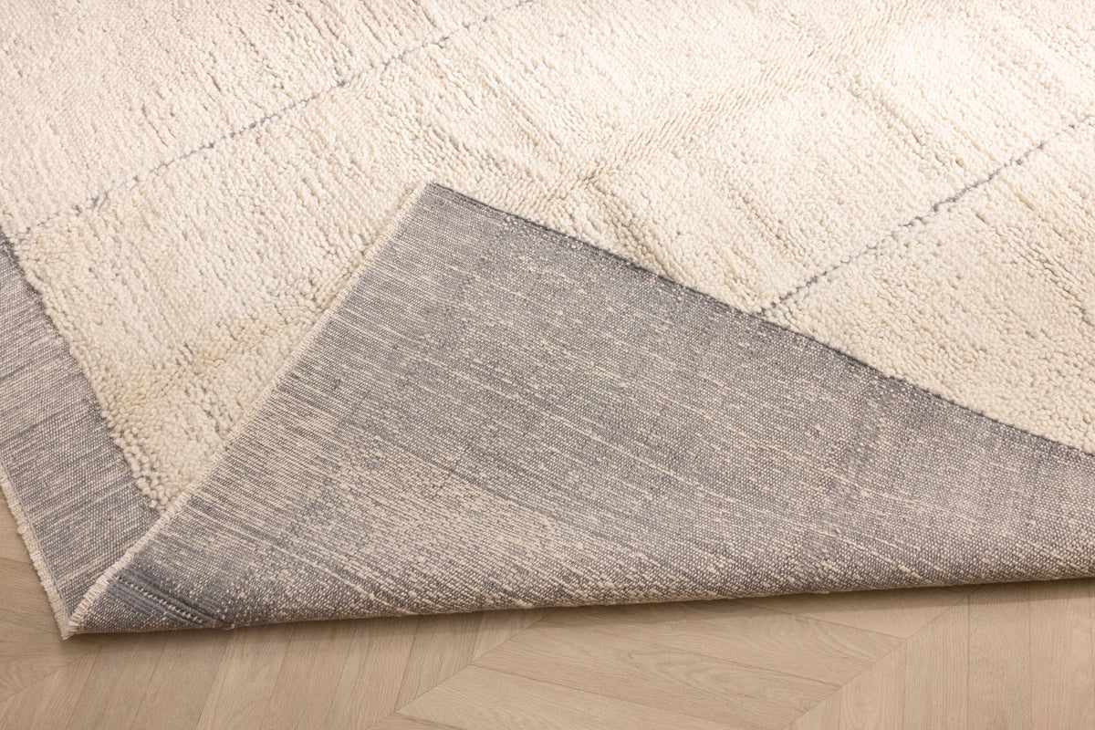 Silver gray shaggy wool rug with a high pile texture and a durable woven cotton backing, showing a folded corner detail.