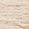 Close-up of a soft, white handwoven shaggy wool rug with a thick, textured high-pile design.