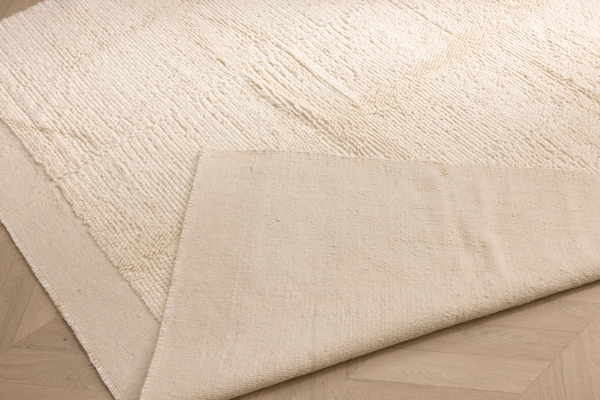 Handwoven white shaggy wool and cotton rug with a thick, textured pile and a smooth, durable backing on a wooden floor.