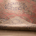 Oversized pink Persian-style wool and cotton rug with floral motifs and a folded corner showing the woven backing.