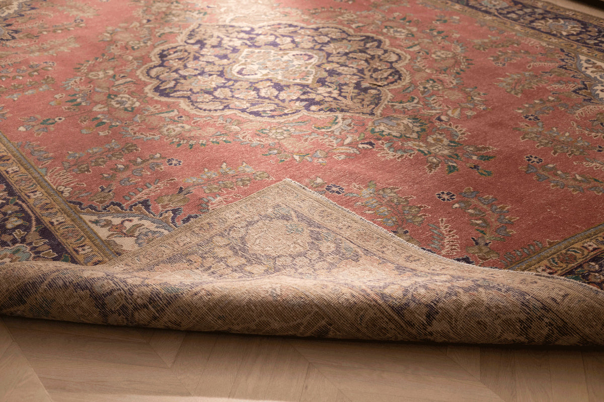 Oversized pink Persian-style wool and cotton rug with floral motifs and a folded corner showing the woven backing.