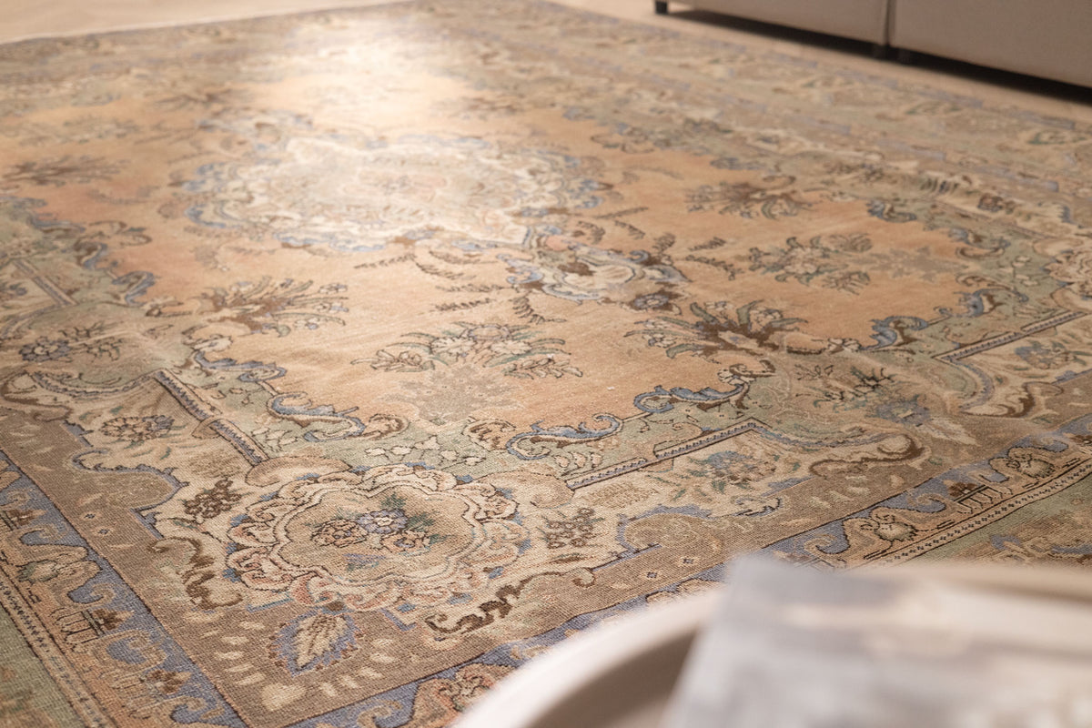 Oversized wool and cotton Persian-style area rug in brown and green with intricate floral motifs and a low pile texture.