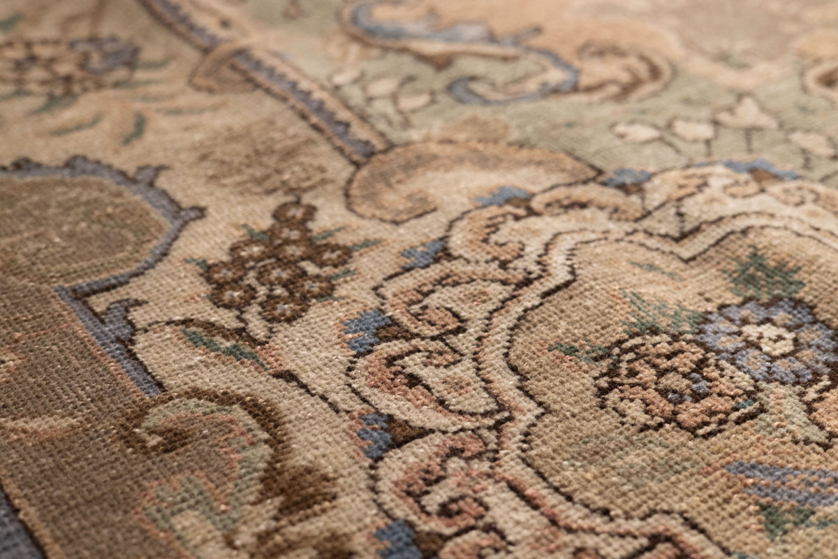 Handmade wool and cotton Persian-style area rug with intricate brown and green floral patterns and low-pile texture.