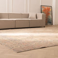 Oversized beige Persian-style wool and cotton area rug with intricate floral motifs in a bright, modern living room.