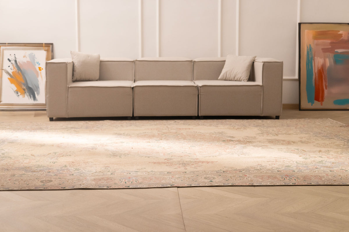 Oversized beige Persian-style wool and cotton area rug with intricate floral motifs in a bright, modern living room.