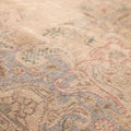 Close-up of a beige, handmade wool and cotton Persian-style rug featuring intricate floral motifs and traditional patterns.