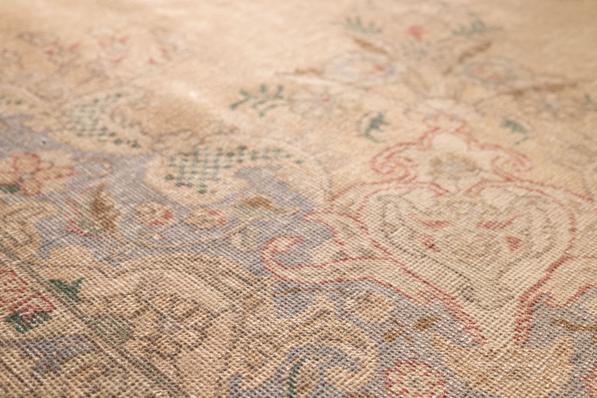Close-up of a beige, handmade wool and cotton Persian-style rug featuring intricate floral motifs and traditional patterns.
