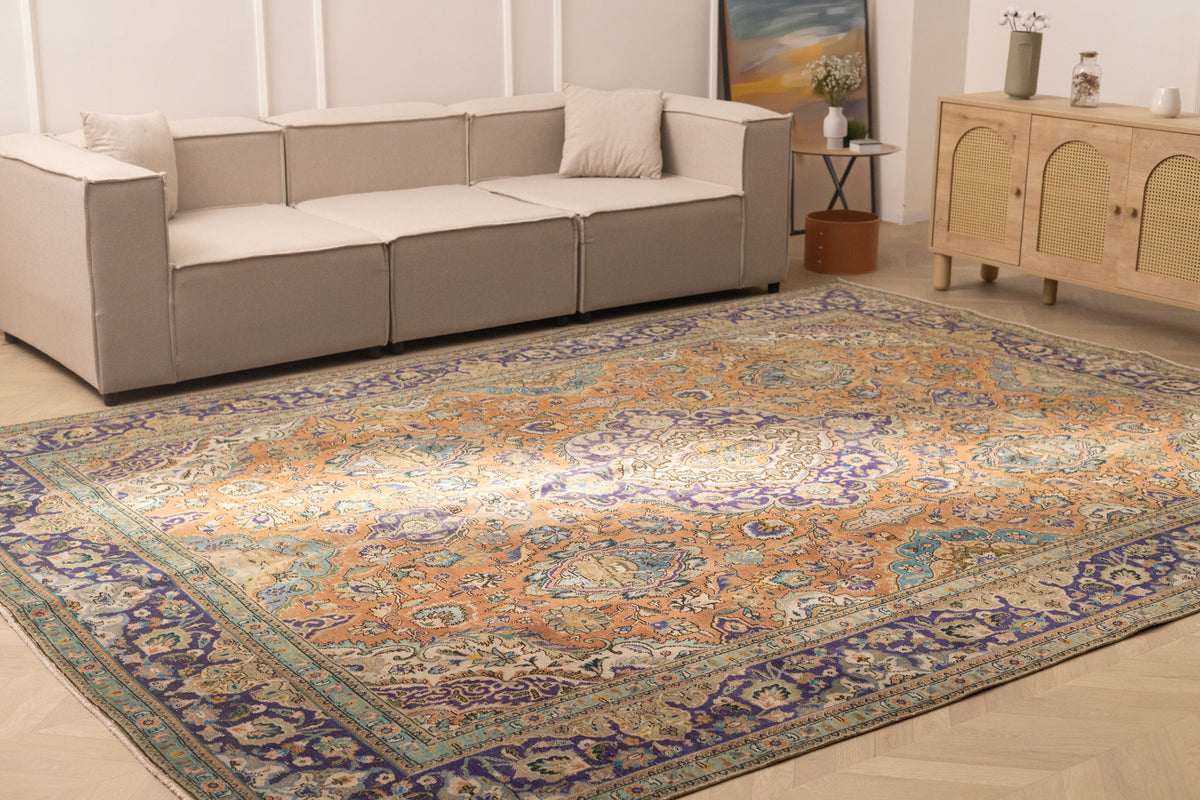 Oversized Persian-style wool and cotton rug with orange and navy floral patterns in a traditional bohemian living room.