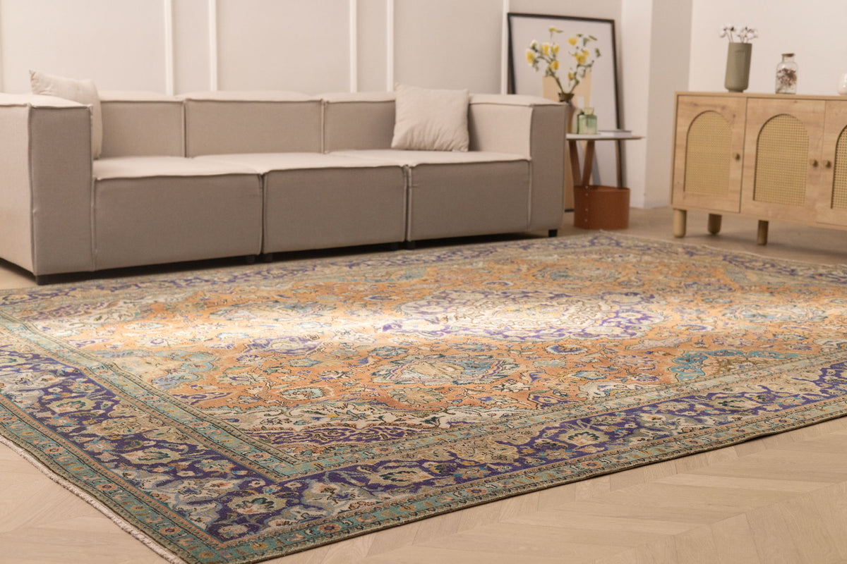 Oversized Persian-style wool and cotton rug with orange and navy floral patterns in a bohemian living room.