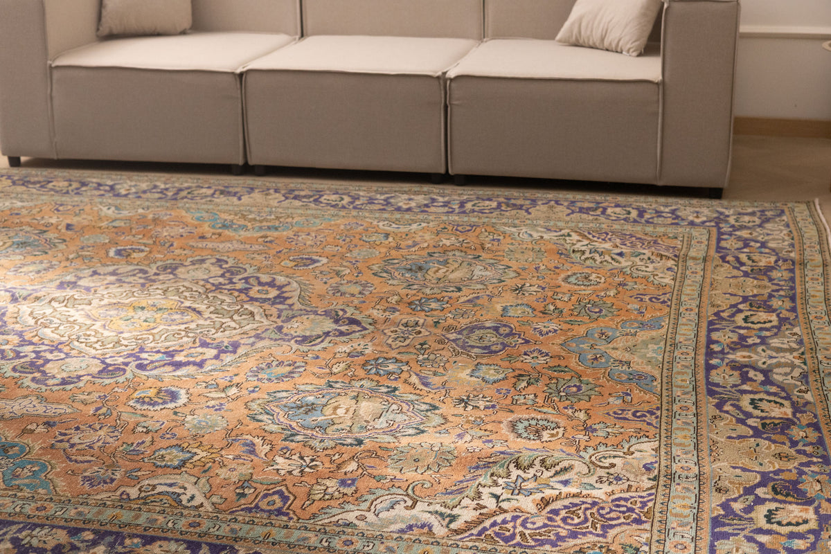Oversized Persian-style wool and cotton rug with orange and navy floral patterns in a traditional bohemian living room.