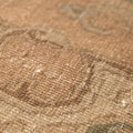 Close-up of a beige and brown Persian-style wool and cotton rug with intricate floral patterns and low pile texture.