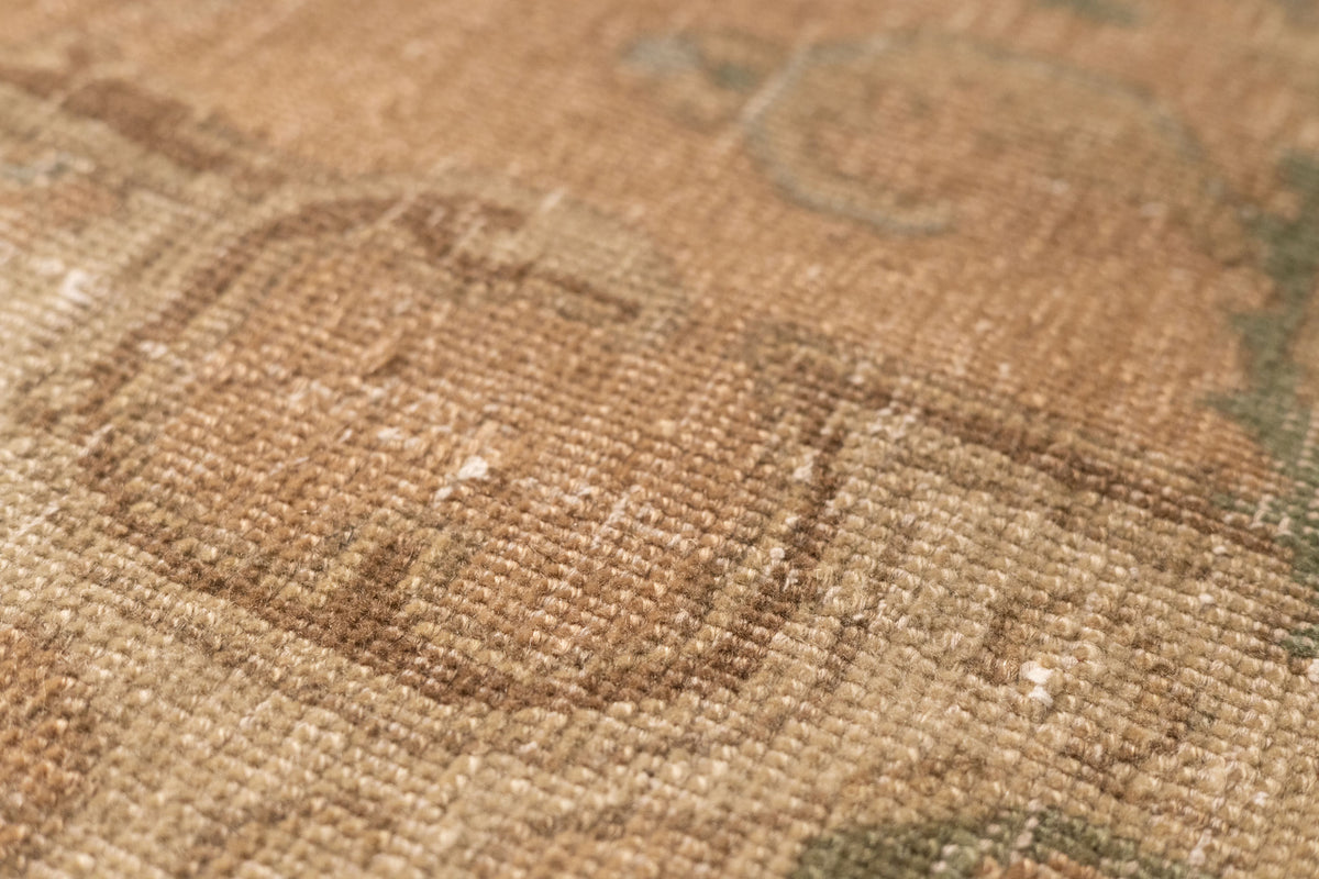 Close-up of a beige and brown Persian-style wool and cotton rug with intricate floral patterns and low pile texture.