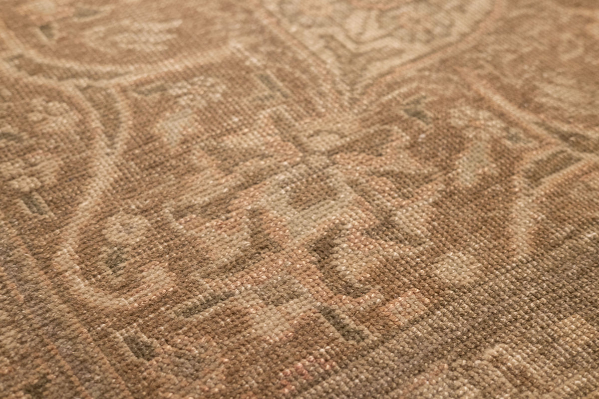 Close-up of a handmade wool and cotton Persian area rug featuring intricate orange and brown floral patterns.