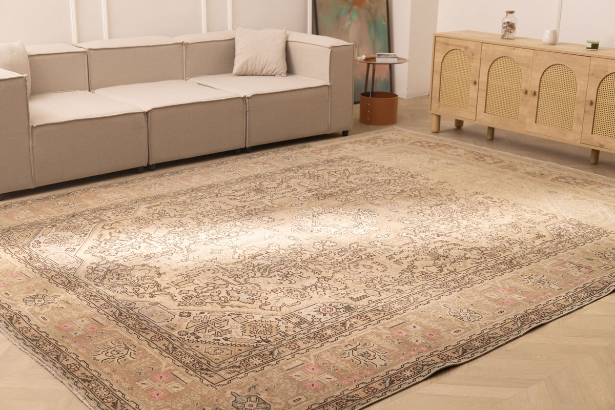 Oversized beige Persian-style wool and cotton area rug featuring intricate geometric and floral motifs in a living room.