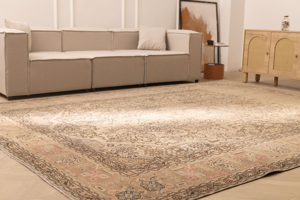 Oversized beige Persian-style wool and cotton rug with intricate geometric and floral patterns in a living room.