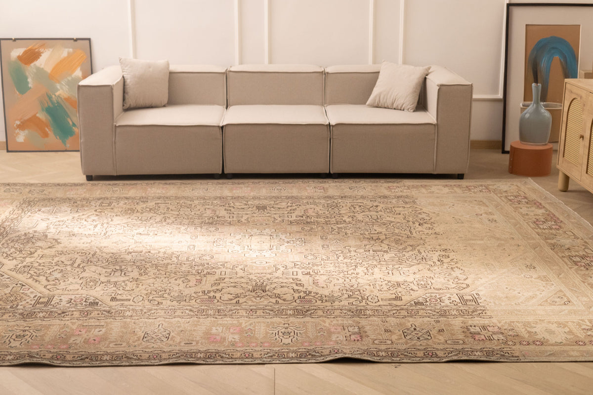 Oversized beige Persian-style wool and cotton rug with intricate geometric and floral patterns in a living room.
