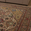 Oversized handmade wool and cotton Persian rug with intricate red, white, and floral bohemian patterns on a light wood floor.