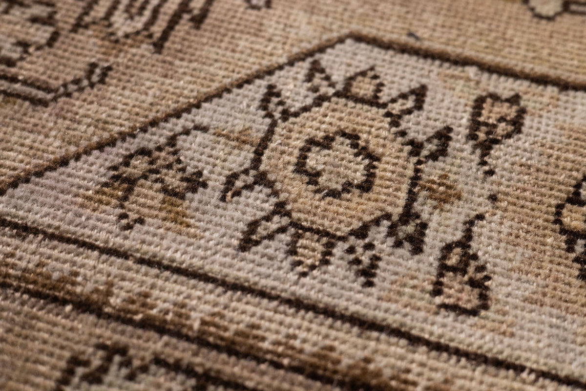 Close-up of a handmade wool and cotton Persian-style rug featuring intricate brown and beige floral motifs.