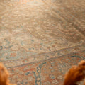 Oversized Persian-style wool and cotton rug in brown and orange with intricate floral patterns and a low-pile texture.