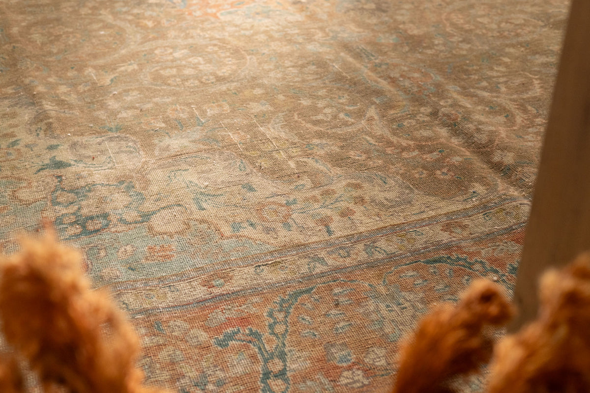 Oversized Persian-style wool and cotton rug in brown and orange with intricate floral patterns and a low-pile texture.