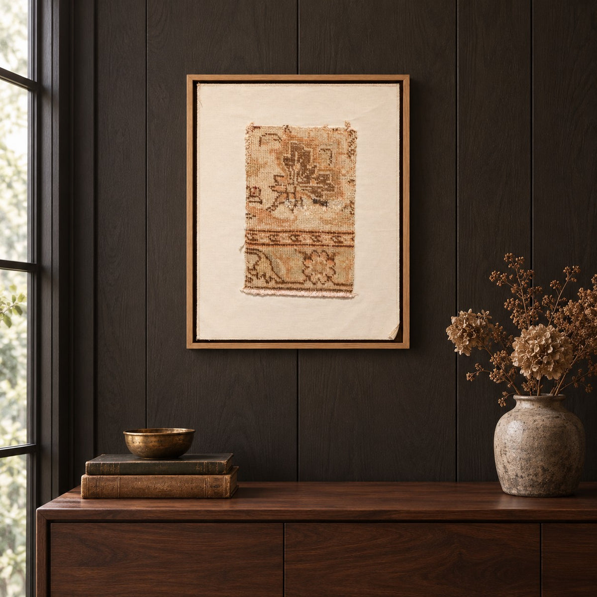 Framed vintage rug fragment wall art in beige, olive, tan hanging on a dark wall above a wooden console