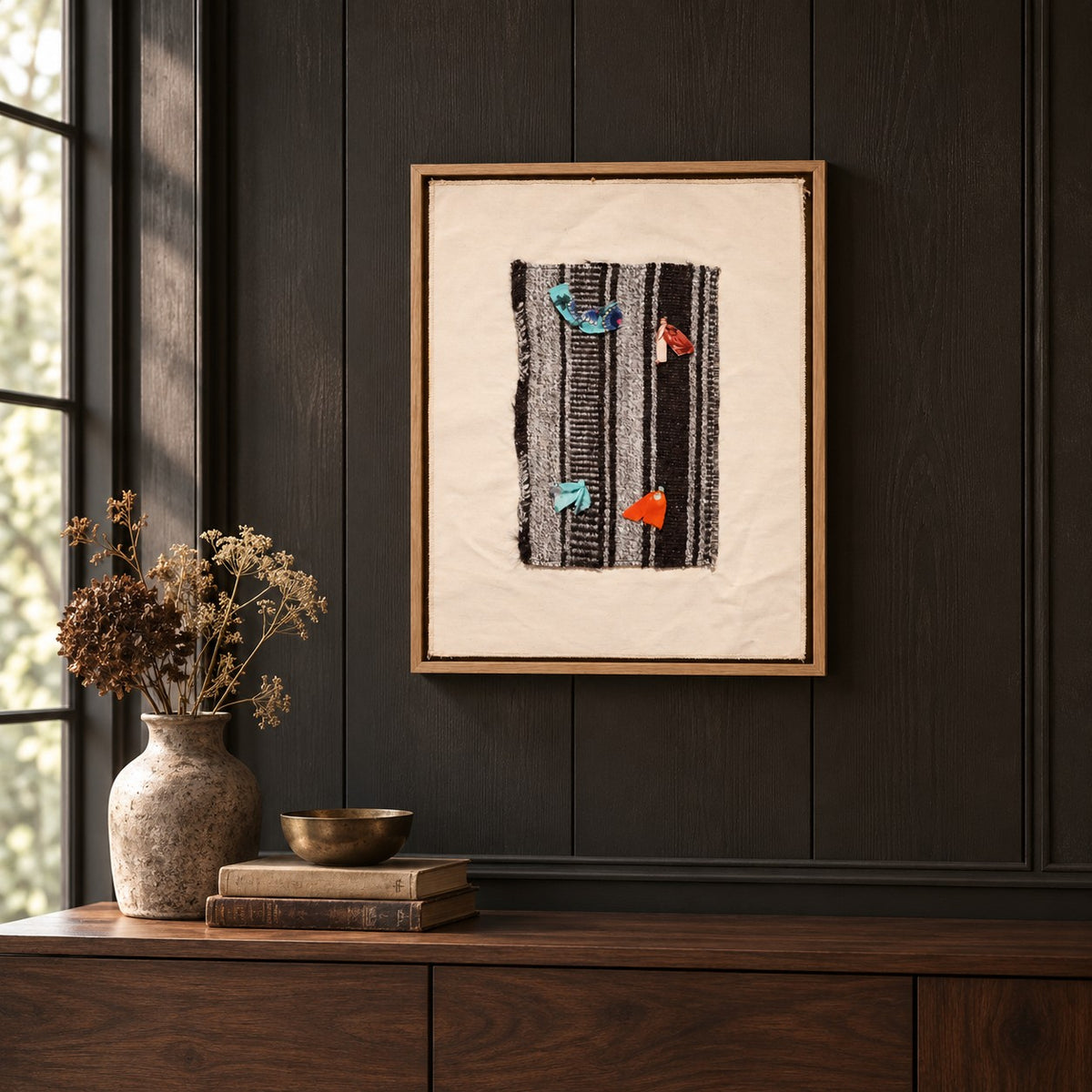 Framed vintage kilim fragment wall art in black, gray, ivory, turquoise, orange hanging on a dark wall above a wooden console