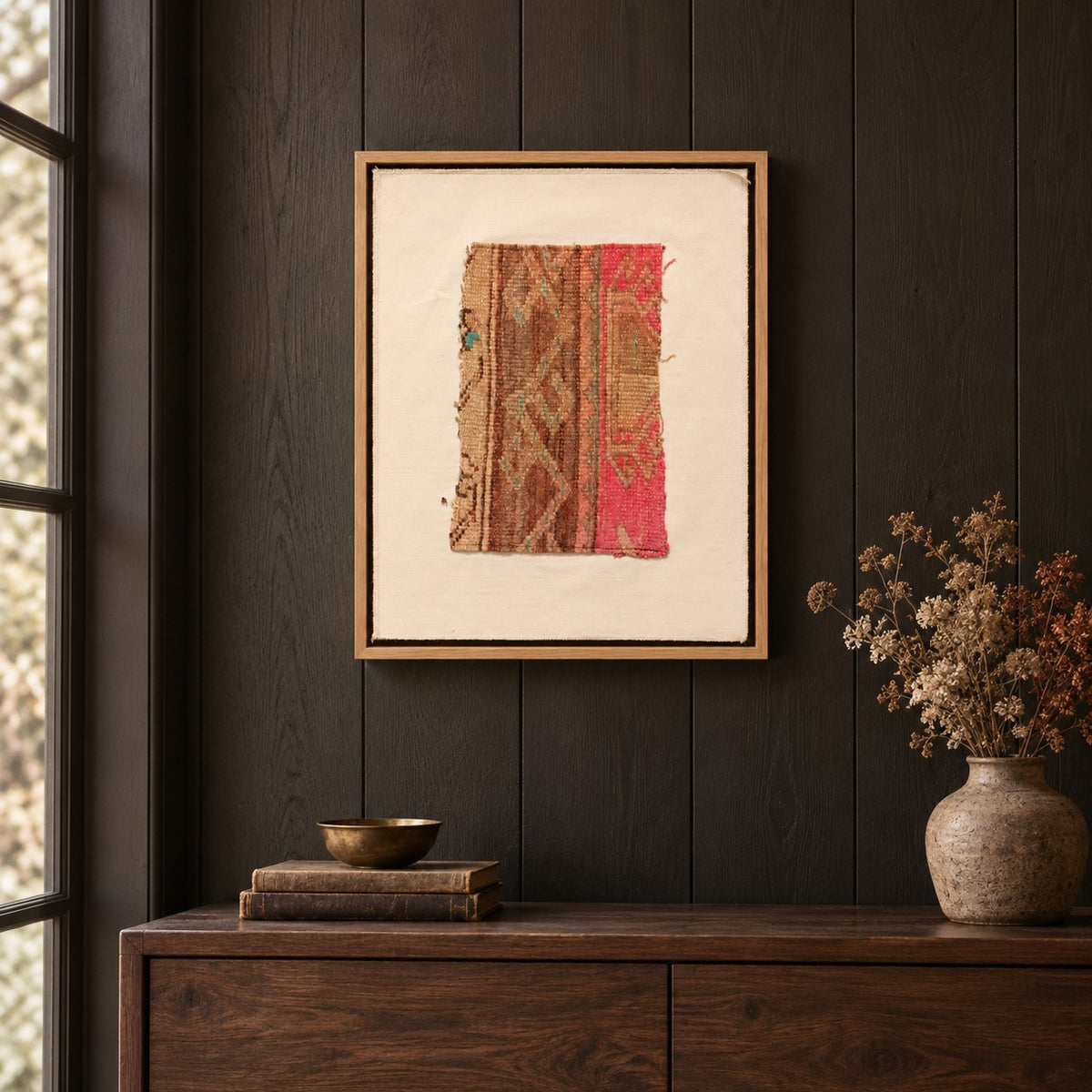 Framed vintage kilim fragment wall art in brown, tan, pink hanging on a dark wall above a wooden console