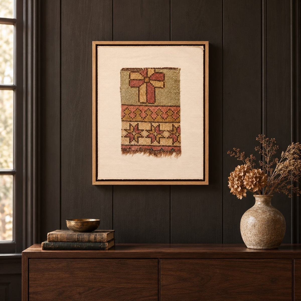 Framed vintage rug fragment wall art in sage, rust, mustard hanging on a dark wall above a wooden console