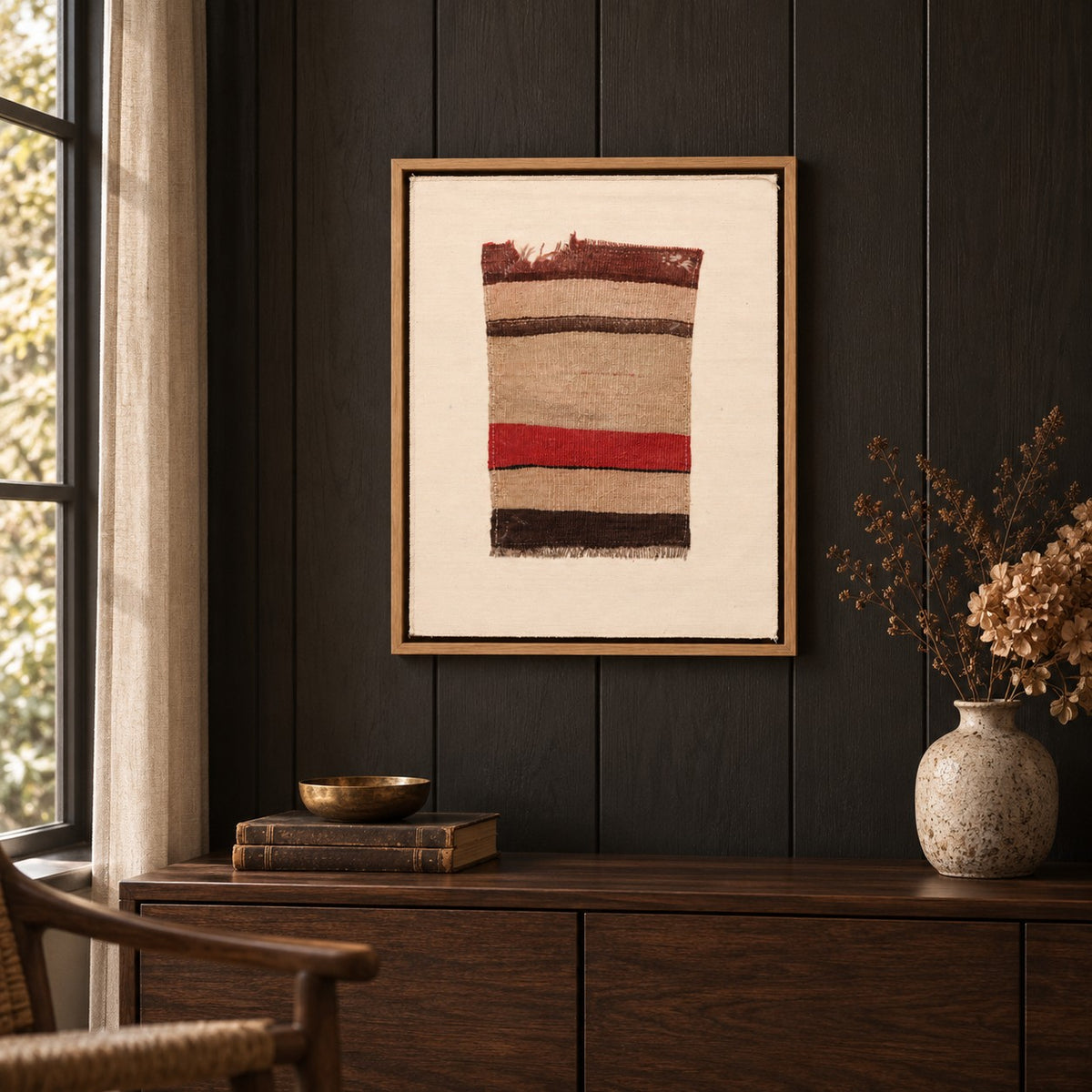 Framed vintage kilim fragment wall art in oatmeal, red, dark brown hanging on a dark wall above a wooden console