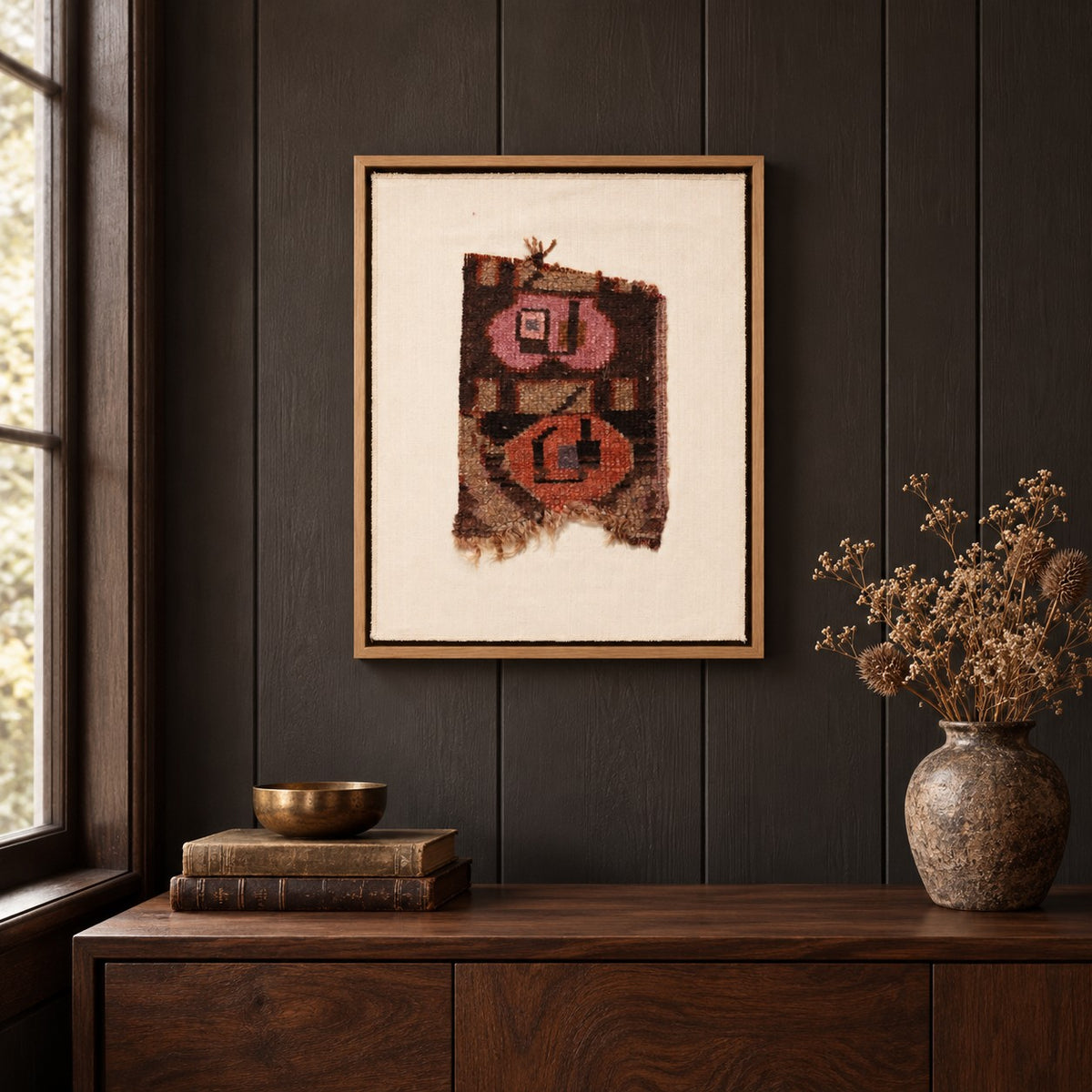 Framed vintage rug fragment wall art in dark brown, pink, orange hanging on a dark wall above a wooden console