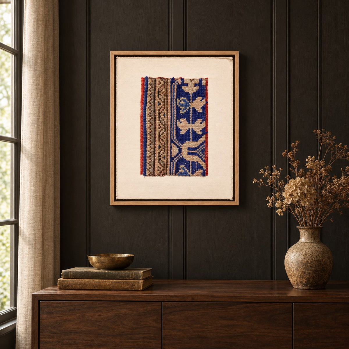 Framed vintage rug fragment wall art in cobalt blue, tan, red hanging on a dark wall above a wooden console