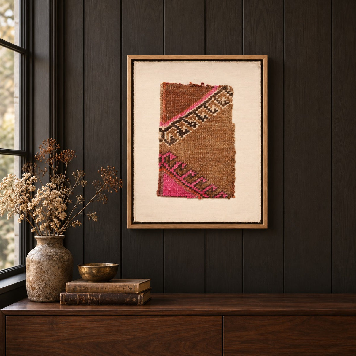 Framed vintage rug fragment wall art in camel, pink, black hanging on a dark wall above a wooden console