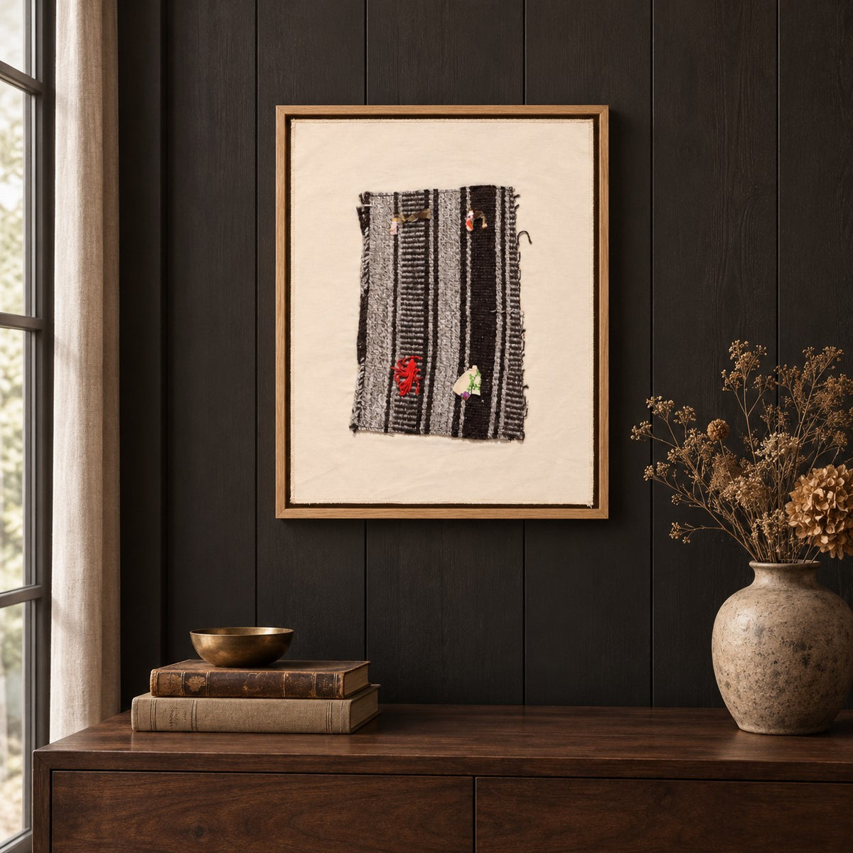 Framed vintage kilim fragment wall art in black, gray, ivory, red hanging on a dark wall above a wooden console