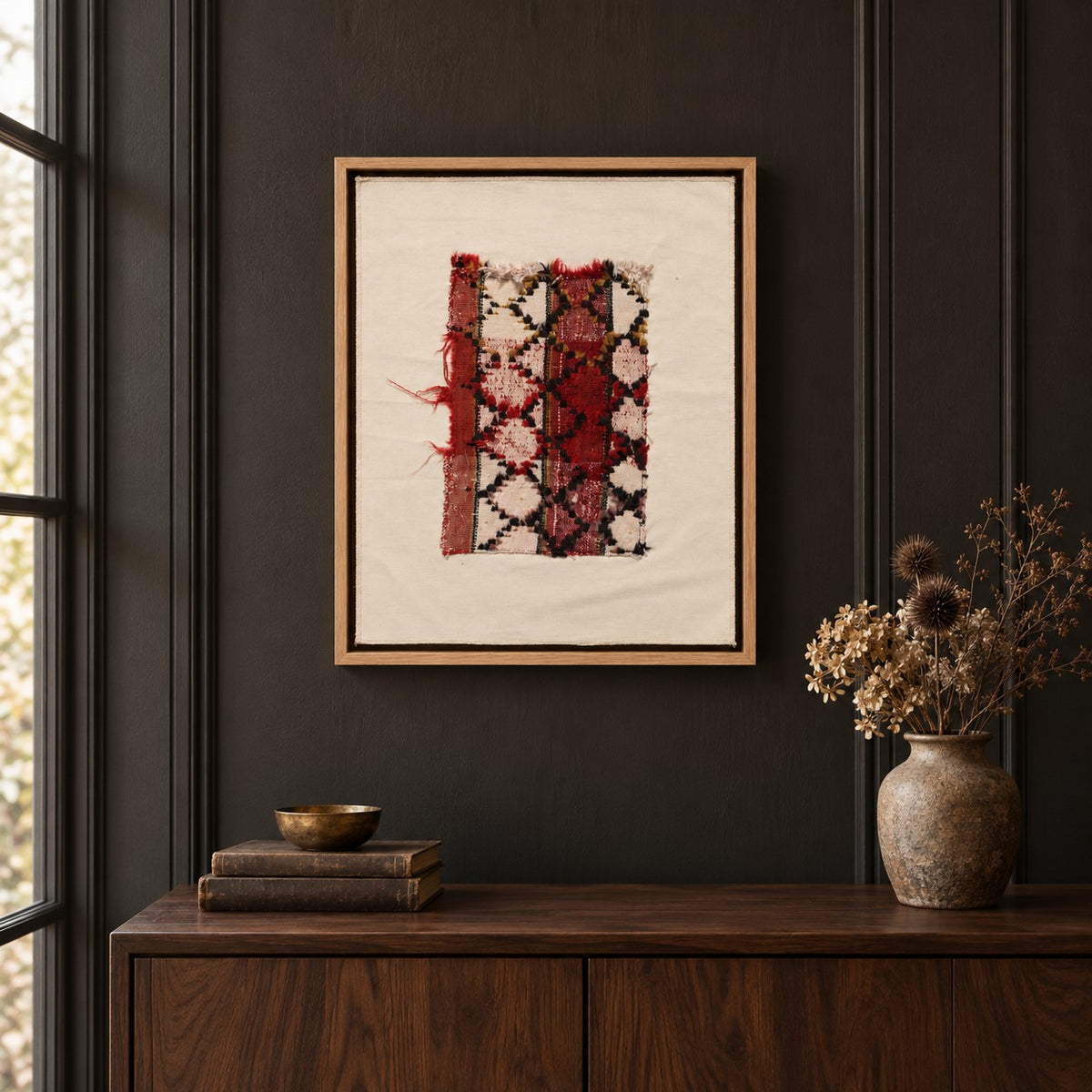 Framed vintage rug fragment wall art in red, ivory, black hanging on a dark wall above a wooden console