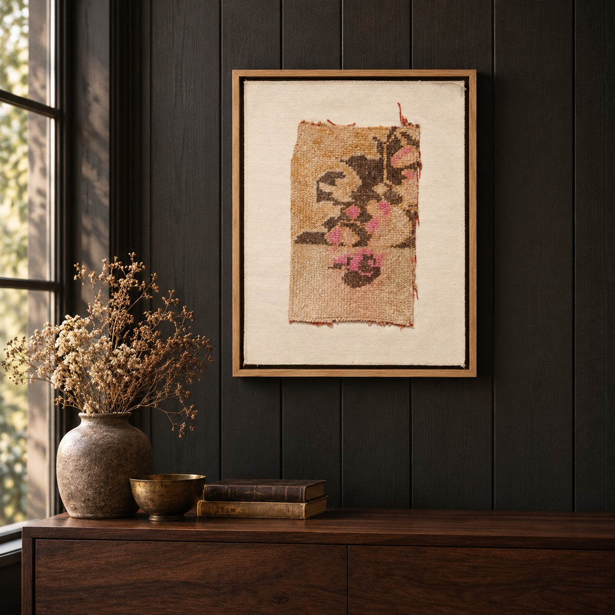 Framed vintage rug fragment wall art in apricot, brown, pink hanging on a dark wall above a wooden console